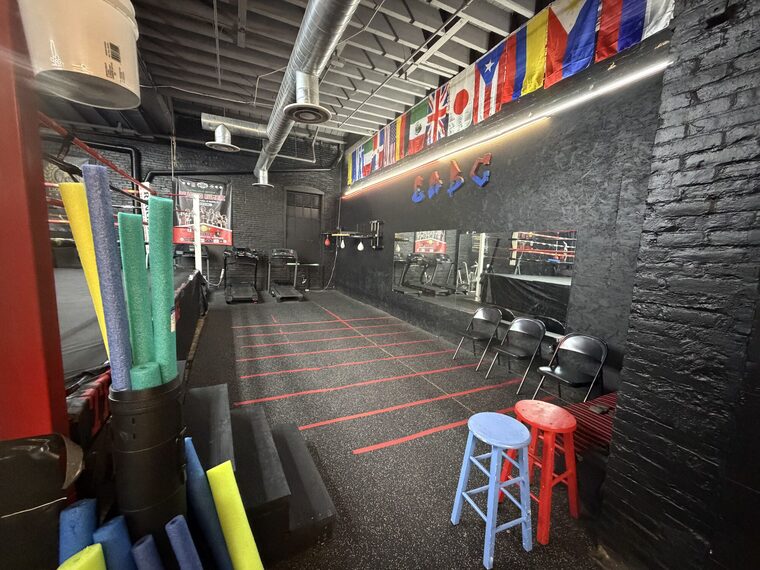 The conditioning end of the gym: foam rollers and mats stacked against a black brick wall painted ERBC, with the flags of members' home countries strung above it.