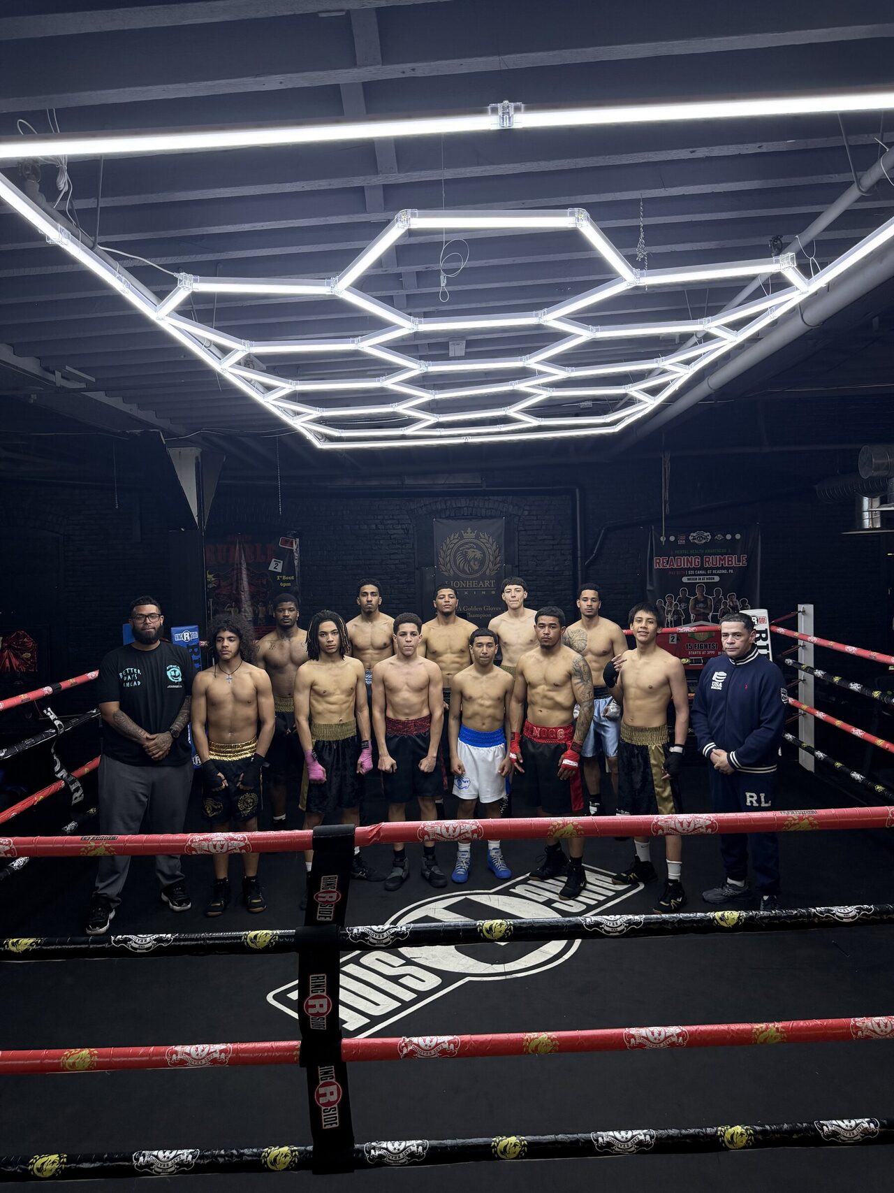 The East Reading Boxing Club amateur team and their two coaches lined up shoulder to shoulder inside the ring, under the gym's hexagonal LED light rig.