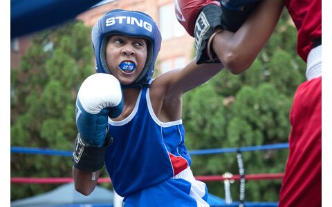 A young fighter in blue slipping under a punch, mouthguard in, headgear on.