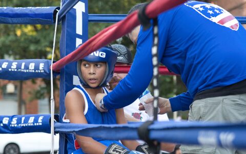 A young fighter resting on the stool in his corner between rounds while his coach talks him through it.