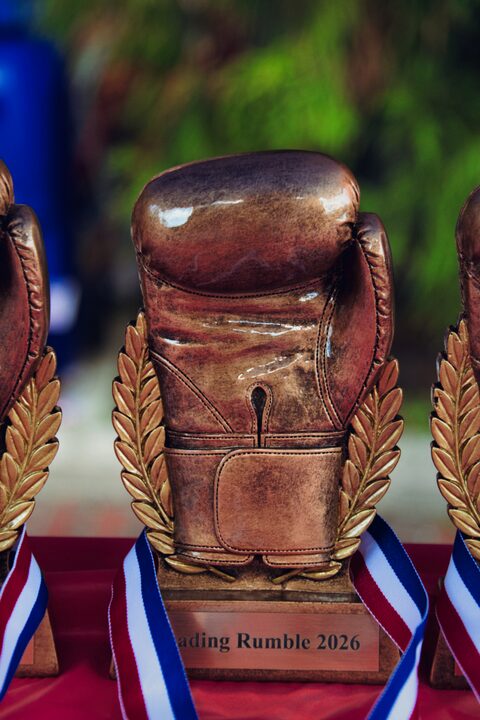 A Reading Rumble 2026 trophy topped with a bronze boxing glove, standing with the ribboned medals on the awards table.