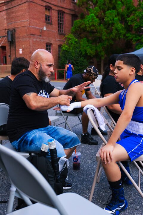 A coach wrapping a young fighter's hands at ringside before a bout.